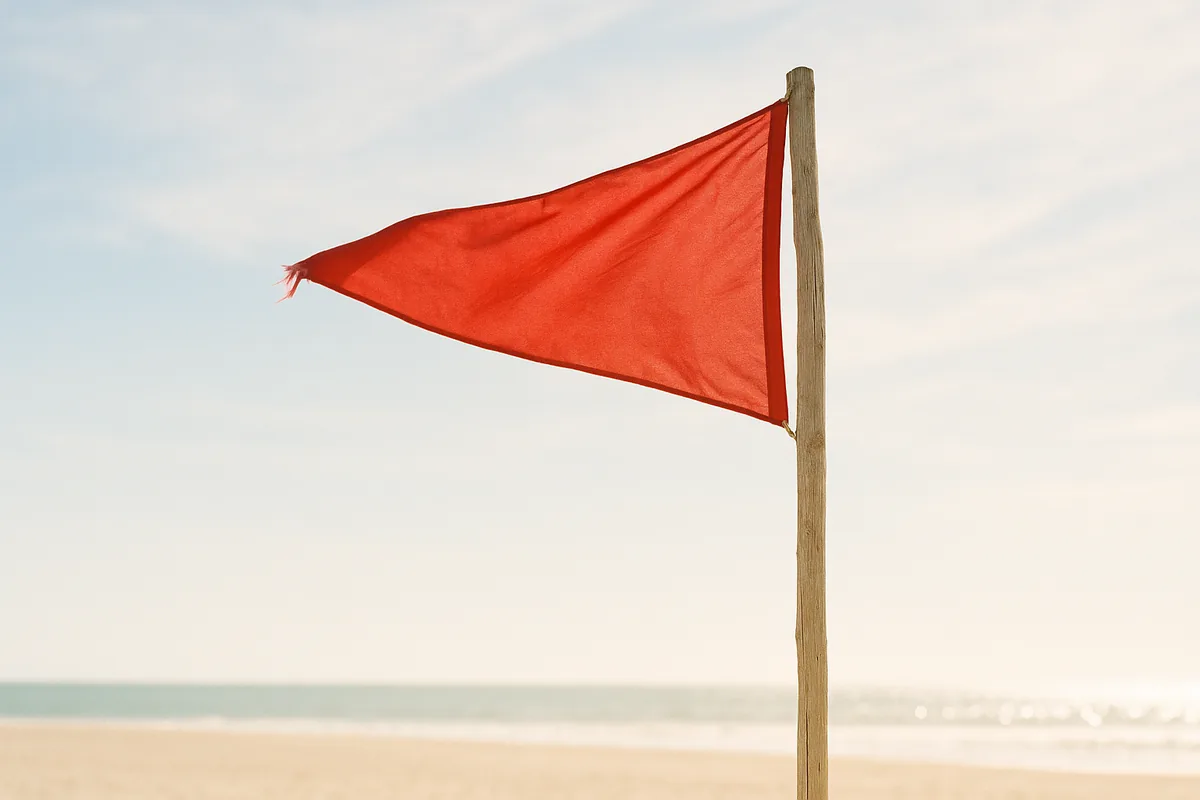 Drapeau rouge de baignade interdite tendu par le vent, en contre-plongée sur un ciel clair