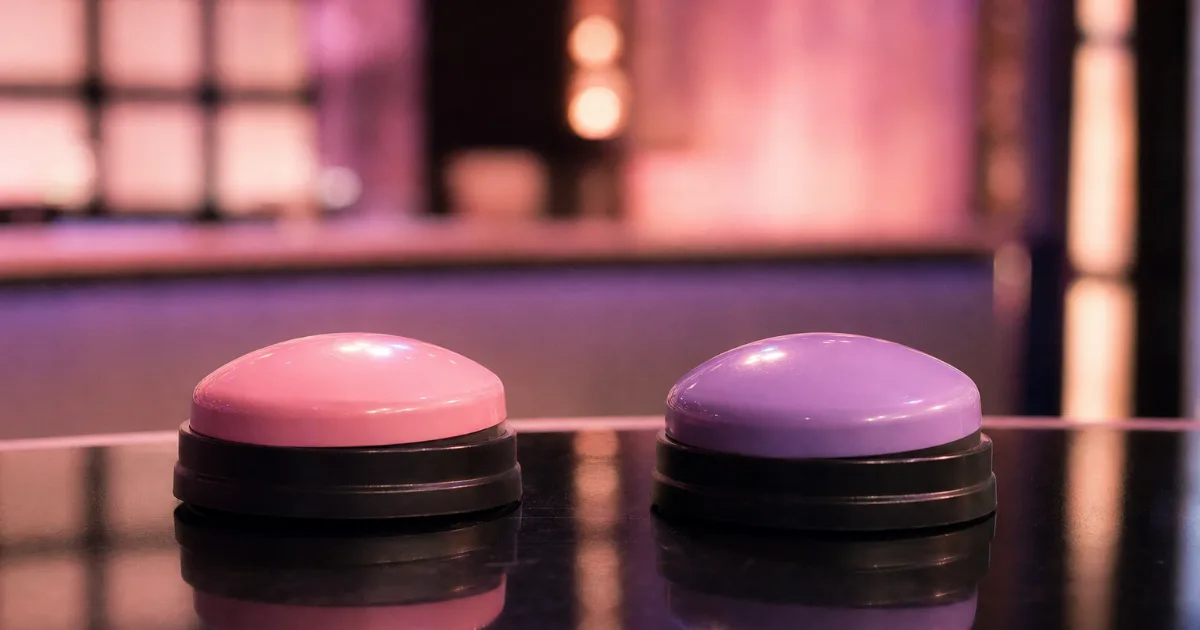 Deux gros boutons de jeu télévisé, un rose et un violet, sur un pupitre brillant sous les lumières d'un plateau