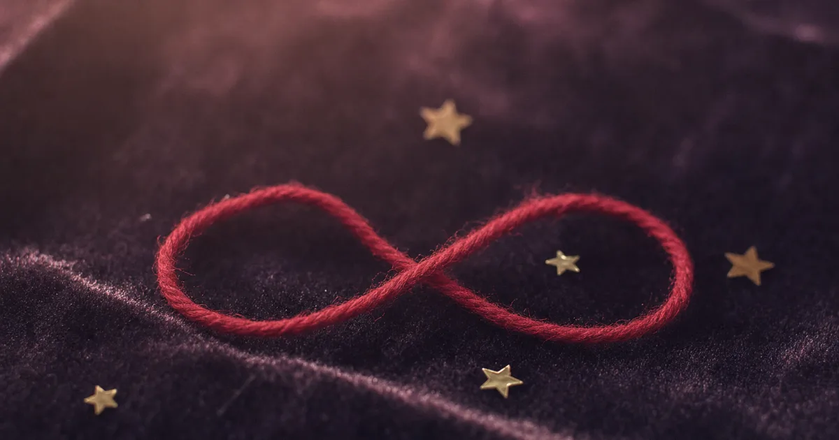 Un fil rouge posé en forme de boucle infinie sur du velours sombre, quelques petites étoiles dorées autour